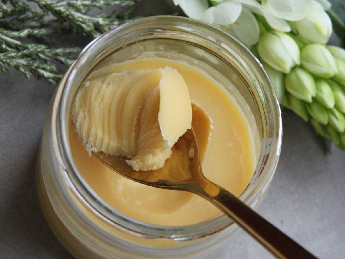 Creamy shea butter in a glass jar with a spoon
