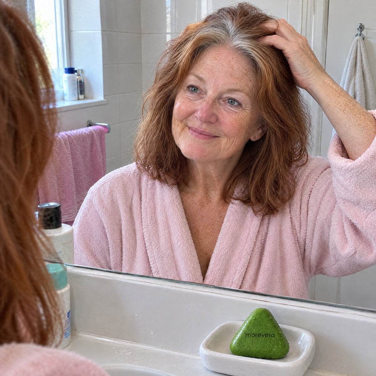 Woman checking the fuller-looking roots at her crown in the bathroom mirror